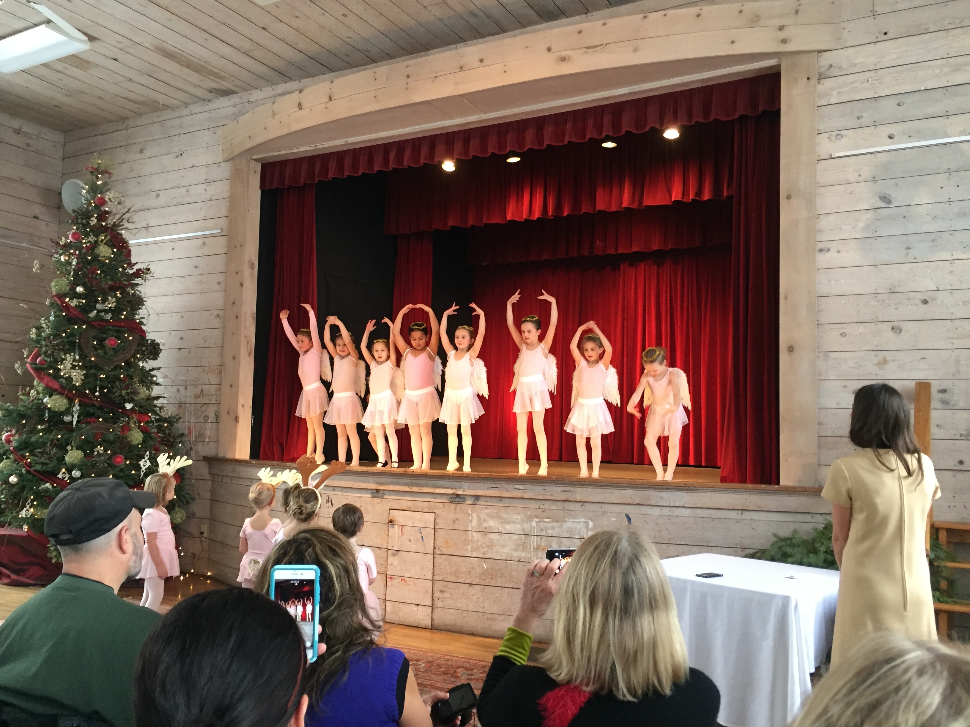 toddler ballarinas on stage at Christmas weaing light pink costumes and holding their arms in the air.