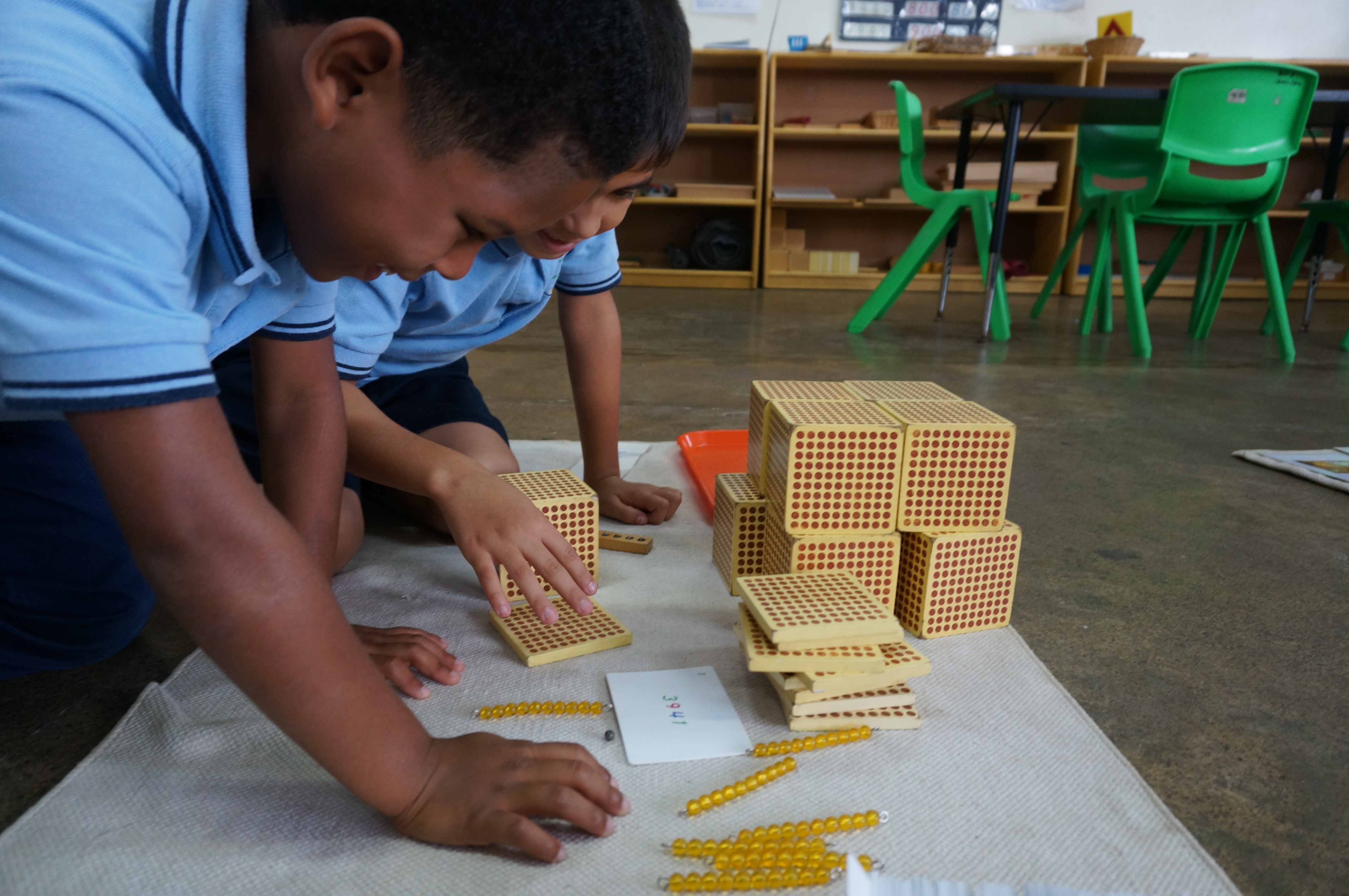 young male students in blue shirts working with blocks that have red dots on each side