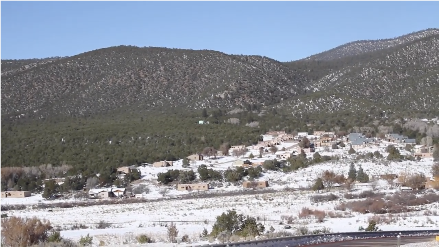 landscape photo of arid terrain. pueblo tyle homes in the foreground, mountains in the background.