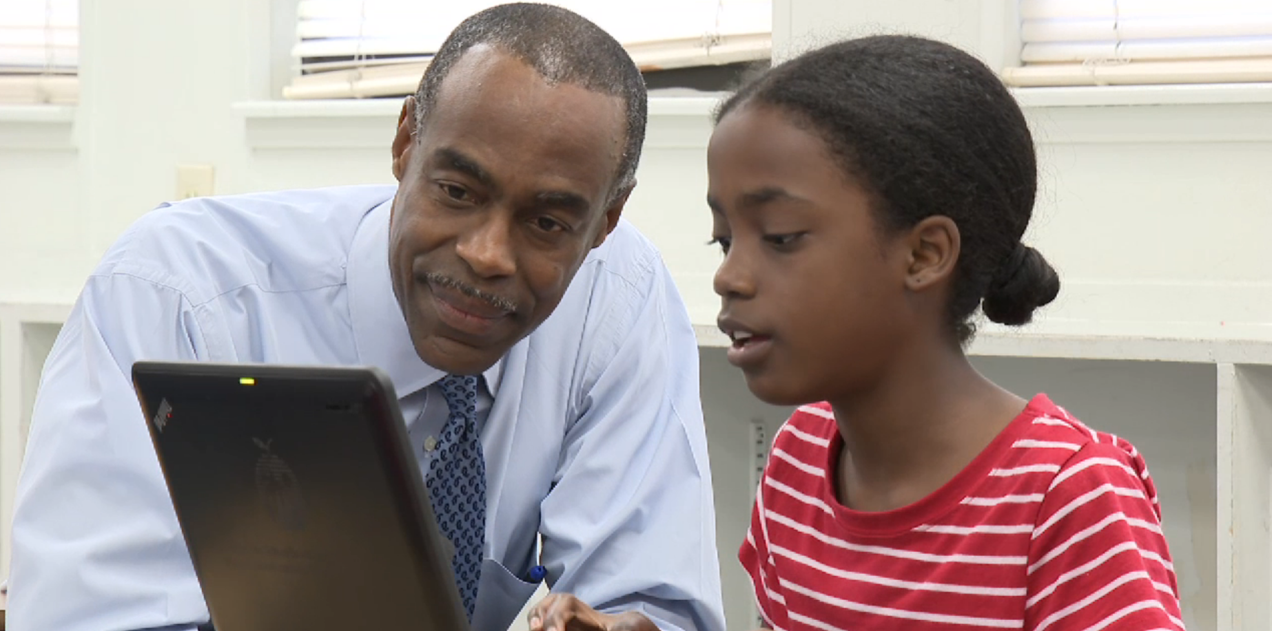 Middle school girl in red shirt with white stripes and male educator looking at a laptop screen. Both are African American.