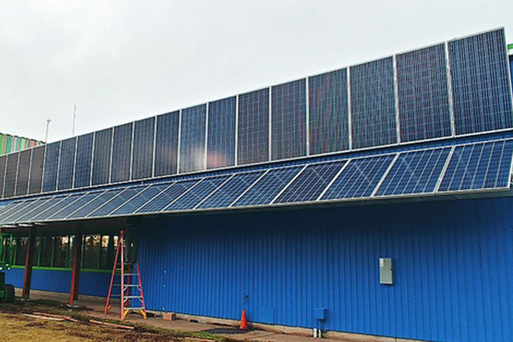 solar panel installation on blue metal building with windows. Solar panels are installed on an angle and also vertically.