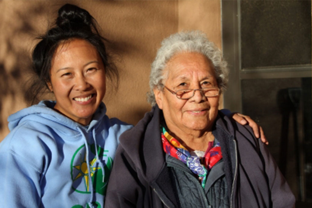Ethnicicy diverse grandmother and grandaughter sitiing together smiling.