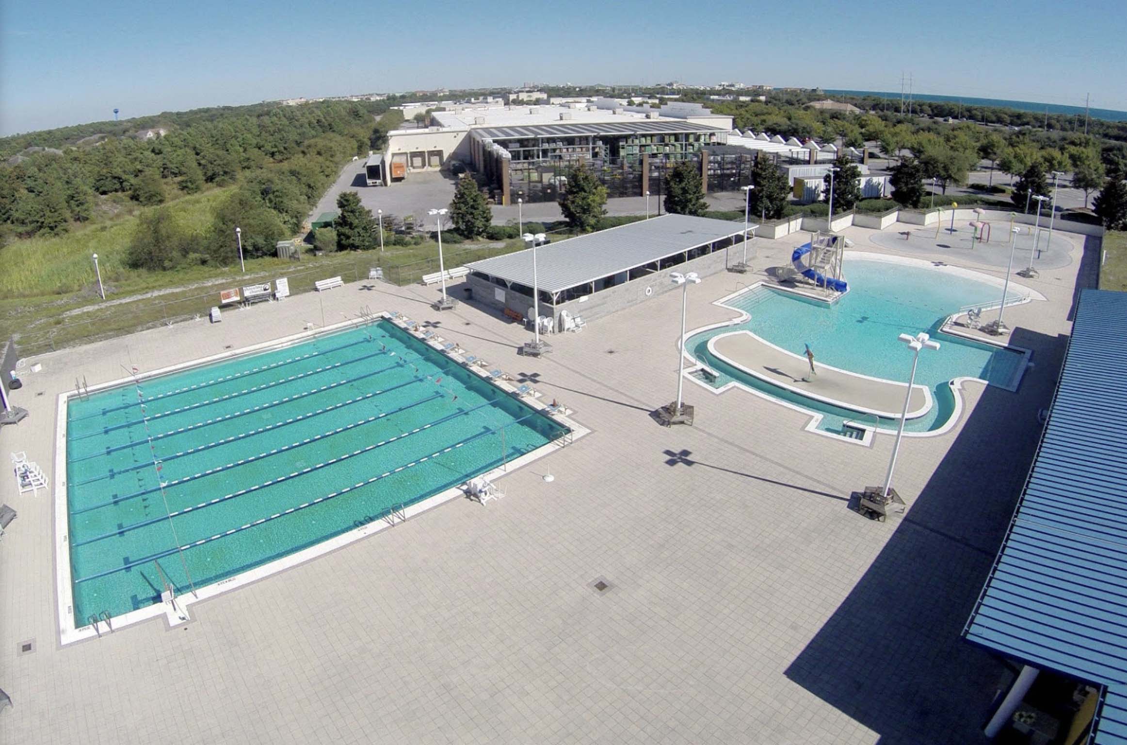 arial photo of 2 outdoor inground pools . One pool has swimming lane separators and the other pool is a round shape with a blue slide.