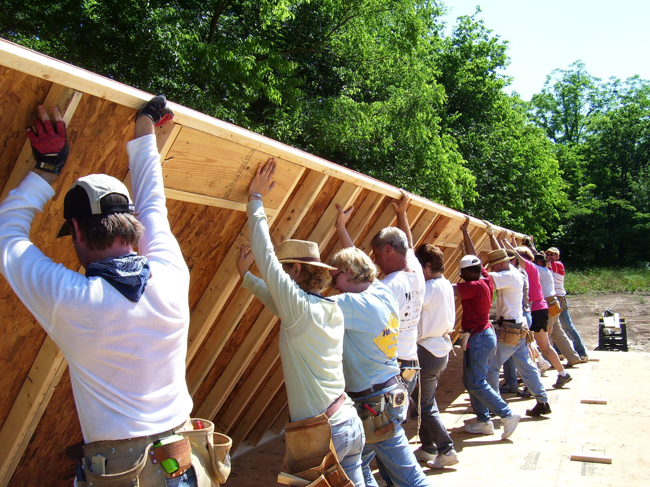 group of people working together to build the side wall of a home